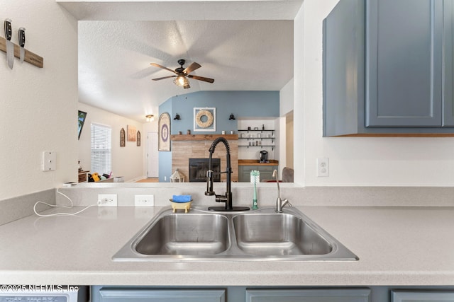 kitchen featuring blue cabinets, lofted ceiling, sink, ceiling fan, and a textured ceiling