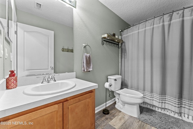 bathroom featuring wood-type flooring, vanity, walk in shower, toilet, and a textured ceiling