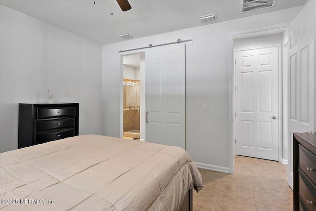 tiled bedroom with a textured ceiling, ceiling fan, connected bathroom, and a barn door