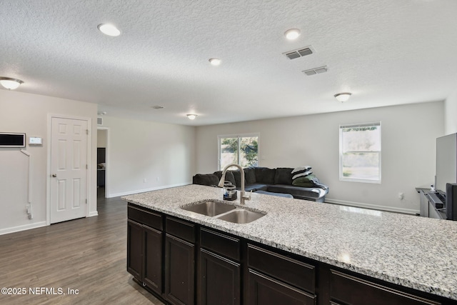 kitchen with dark hardwood / wood-style flooring, light stone countertops, a textured ceiling, dark brown cabinetry, and sink