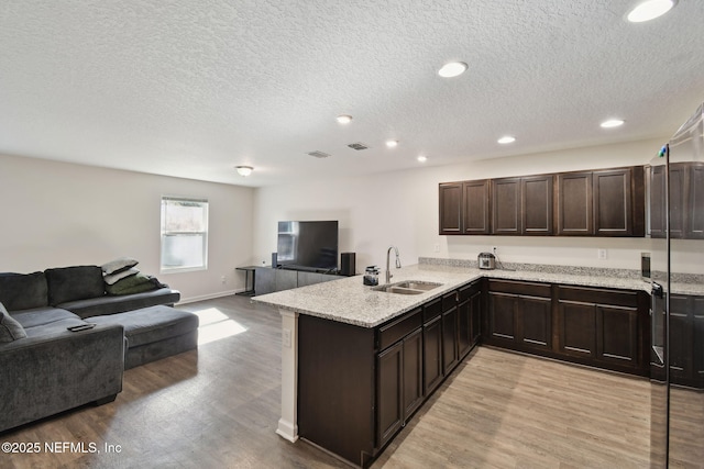 kitchen with light wood-type flooring, kitchen peninsula, dark brown cabinets, and sink