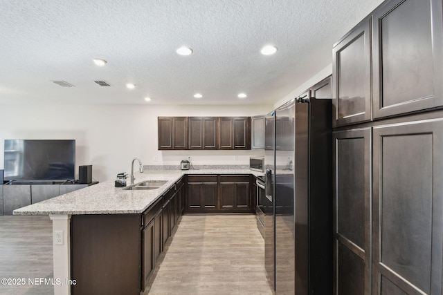 kitchen with kitchen peninsula, light stone counters, light hardwood / wood-style flooring, dark brown cabinetry, and sink