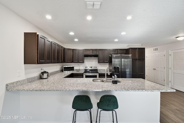 kitchen featuring dark brown cabinetry, appliances with stainless steel finishes, a kitchen bar, sink, and kitchen peninsula