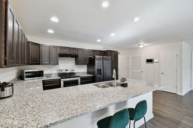 kitchen with a kitchen bar, kitchen peninsula, stainless steel appliances, dark brown cabinetry, and sink