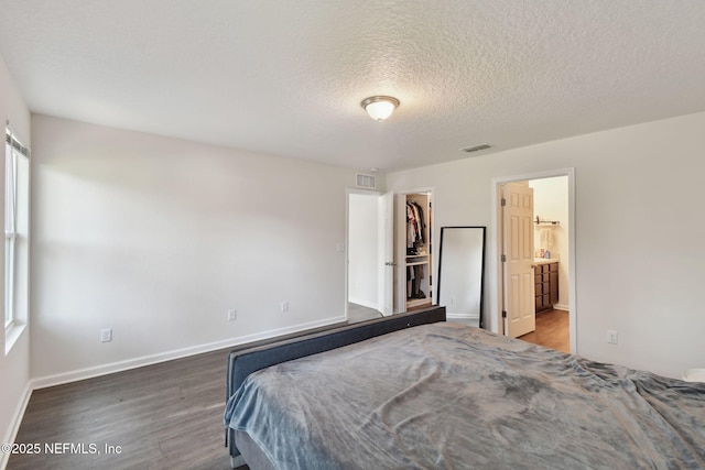 bedroom featuring a spacious closet, connected bathroom, a closet, dark hardwood / wood-style flooring, and a textured ceiling