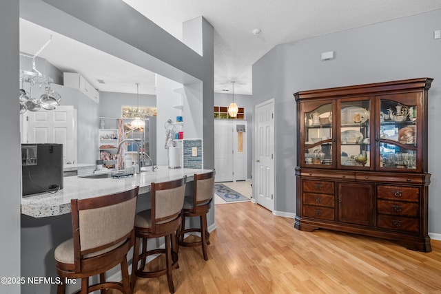 kitchen featuring kitchen peninsula, decorative light fixtures, light stone countertops, light hardwood / wood-style flooring, and a breakfast bar