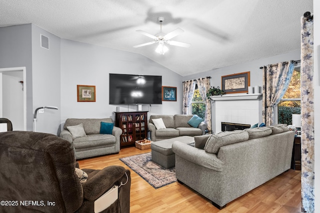 living room with a textured ceiling, a tiled fireplace, lofted ceiling, and hardwood / wood-style floors