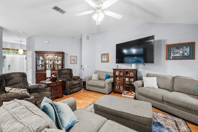 living room with ceiling fan, light wood-type flooring, vaulted ceiling, and a textured ceiling