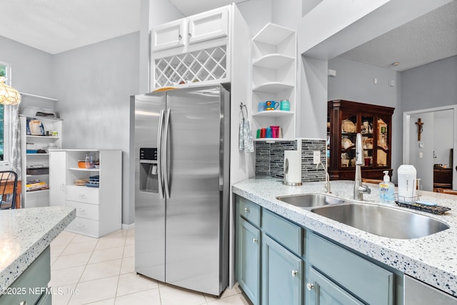 kitchen with stainless steel refrigerator with ice dispenser, decorative backsplash, light stone countertops, light tile patterned floors, and blue cabinets