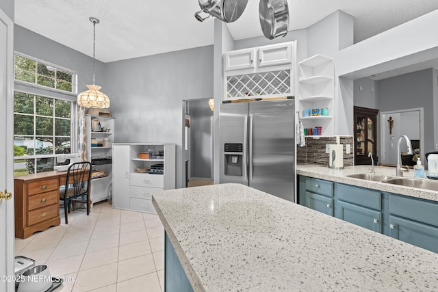 kitchen with pendant lighting, tasteful backsplash, sink, stainless steel fridge, and blue cabinets