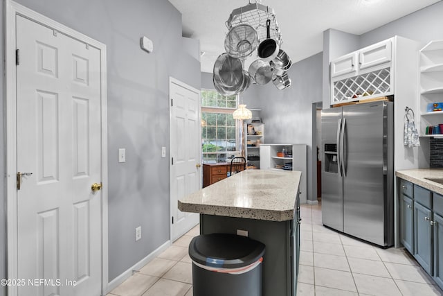 kitchen with stainless steel refrigerator with ice dispenser, white cabinets, light tile patterned floors, and a kitchen island