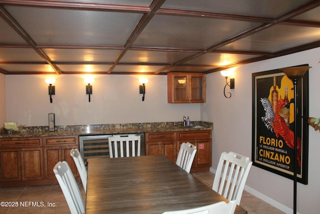 bar with light tile patterned flooring, sink, coffered ceiling, and dark stone countertops