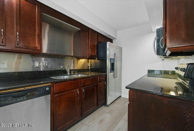 kitchen featuring appliances with stainless steel finishes, dark stone countertops, light hardwood / wood-style flooring, and sink