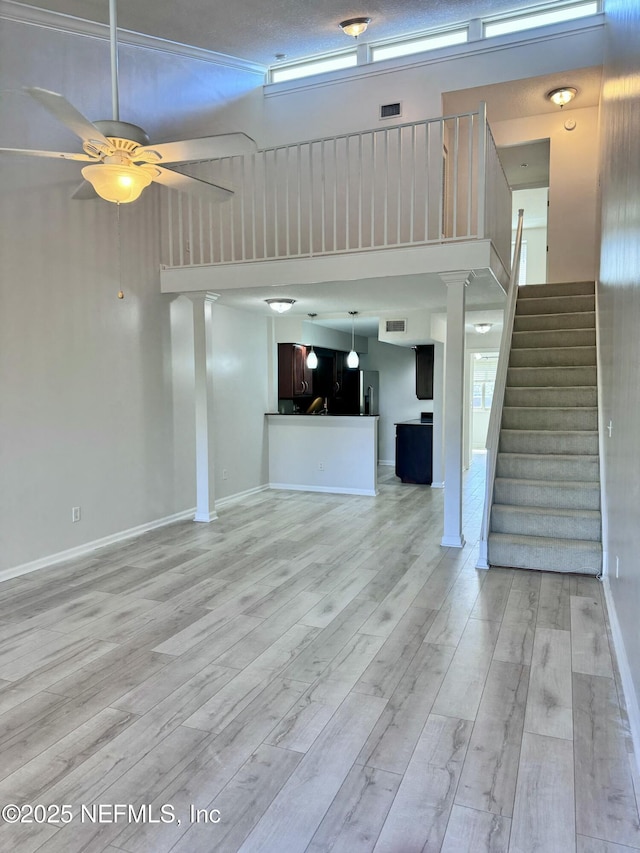 unfurnished living room featuring ceiling fan, light hardwood / wood-style flooring, and a towering ceiling