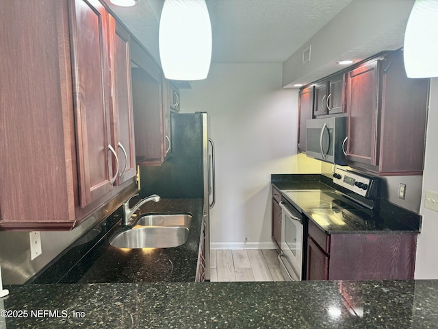 kitchen with appliances with stainless steel finishes, sink, dark stone countertops, and a textured ceiling