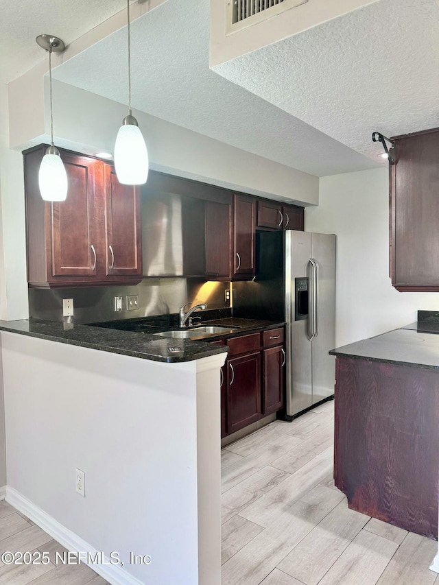 kitchen featuring pendant lighting, a textured ceiling, sink, stainless steel fridge, and kitchen peninsula