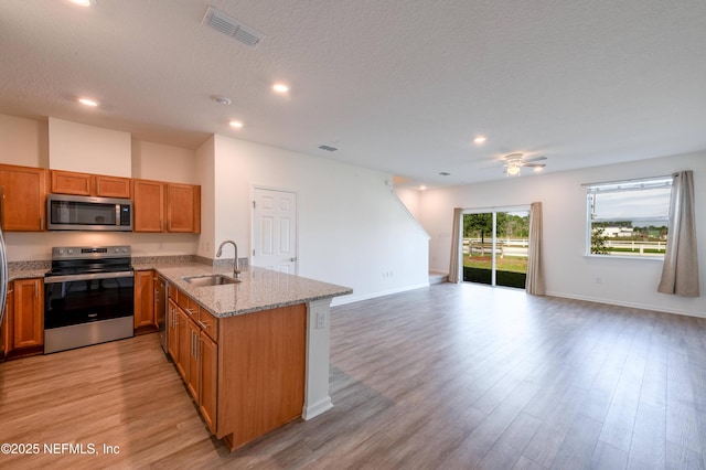 kitchen with sink, light hardwood / wood-style flooring, appliances with stainless steel finishes, light stone countertops, and kitchen peninsula