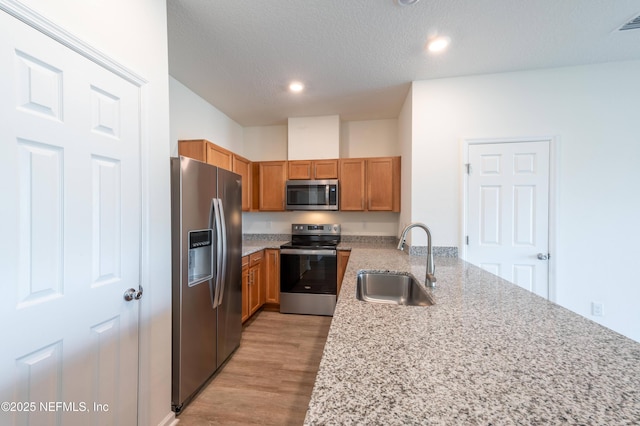 kitchen with sink, kitchen peninsula, stainless steel appliances, light stone countertops, and light hardwood / wood-style flooring