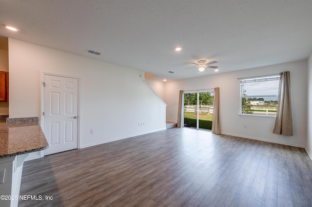 unfurnished living room featuring dark wood-type flooring, ceiling fan, and a textured ceiling