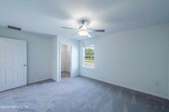 unfurnished bedroom featuring ceiling fan, carpet flooring, a textured ceiling, a spacious closet, and a closet