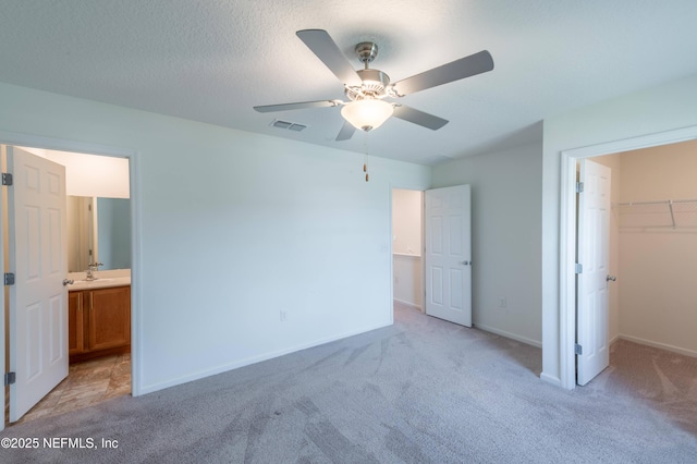 unfurnished bedroom with a walk in closet, a closet, light carpet, and a textured ceiling