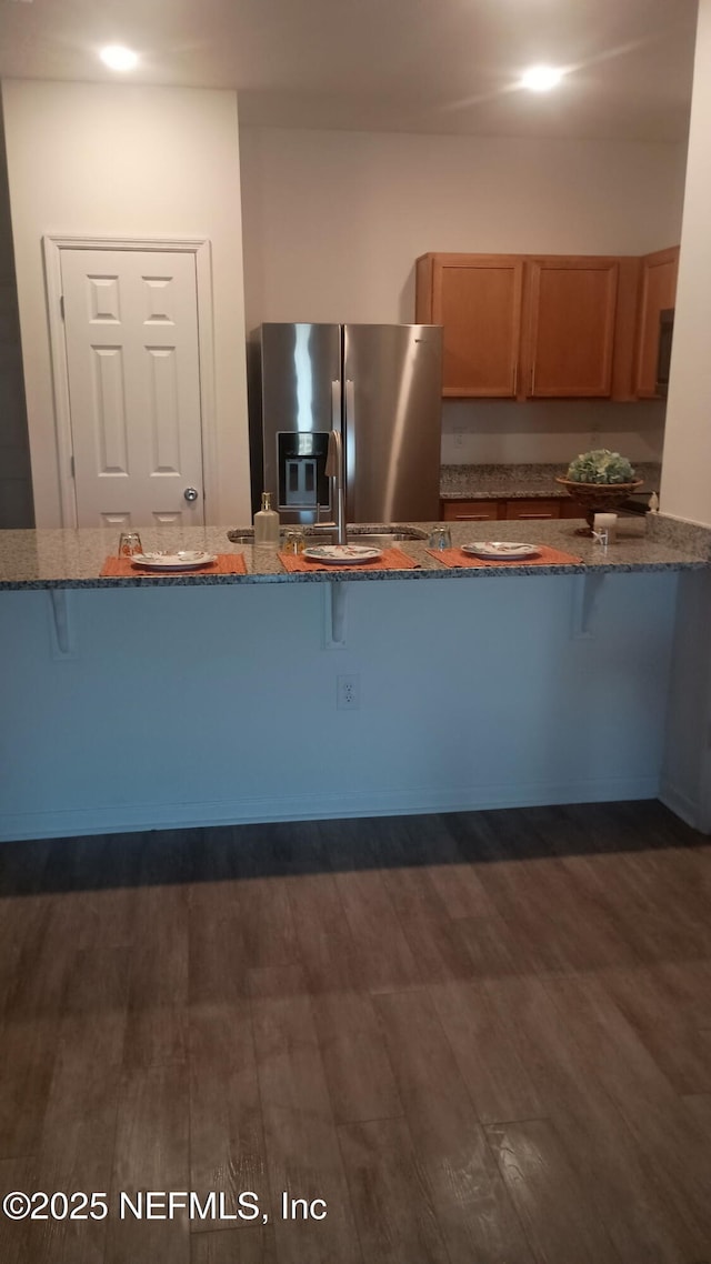 kitchen featuring a kitchen bar, dark hardwood / wood-style flooring, stainless steel fridge with ice dispenser, and dark stone countertops