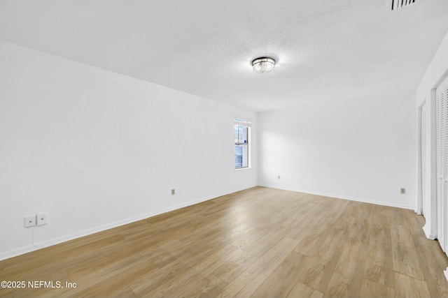 empty room with a textured ceiling and light hardwood / wood-style flooring