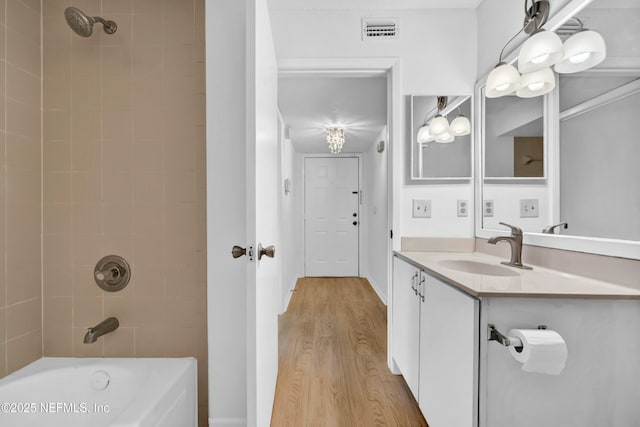 bathroom with hardwood / wood-style floors, vanity, and tiled shower / bath