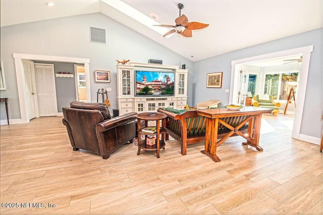 living room featuring ceiling fan, light hardwood / wood-style floors, and vaulted ceiling with skylight