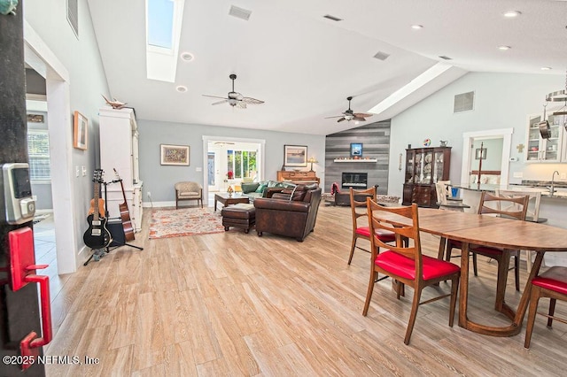 dining space with ceiling fan, vaulted ceiling with skylight, light hardwood / wood-style floors, and a tiled fireplace