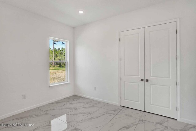 unfurnished bedroom with a closet, recessed lighting, marble finish floor, and baseboards