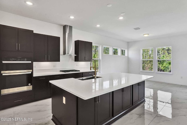 kitchen featuring black stovetop, stainless steel double oven, marble finish floor, wall chimney exhaust hood, and a sink