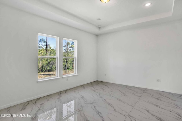 unfurnished room featuring recessed lighting, marble finish floor, a raised ceiling, and baseboards