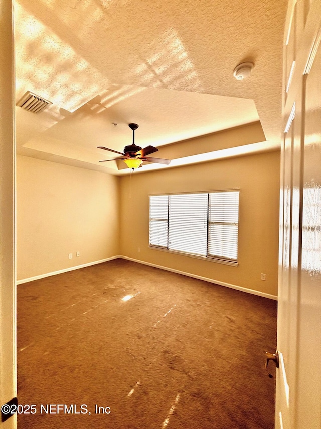 spare room with a textured ceiling, ceiling fan, carpet, and a raised ceiling