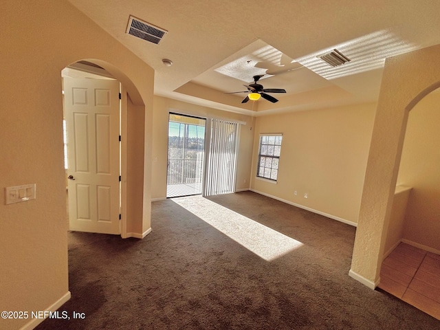 spare room with ceiling fan, dark carpet, and a raised ceiling