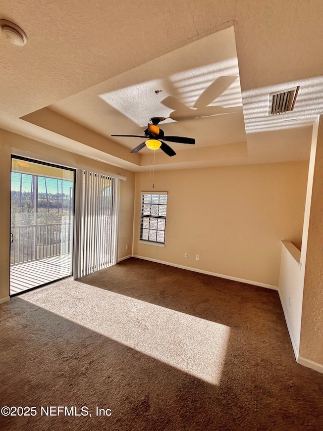 unfurnished room with ceiling fan, a tray ceiling, a textured ceiling, and dark colored carpet