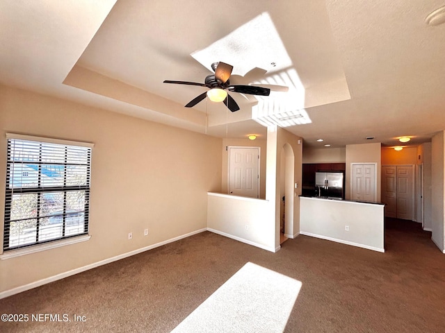 unfurnished living room featuring ceiling fan, dark carpet, and a raised ceiling