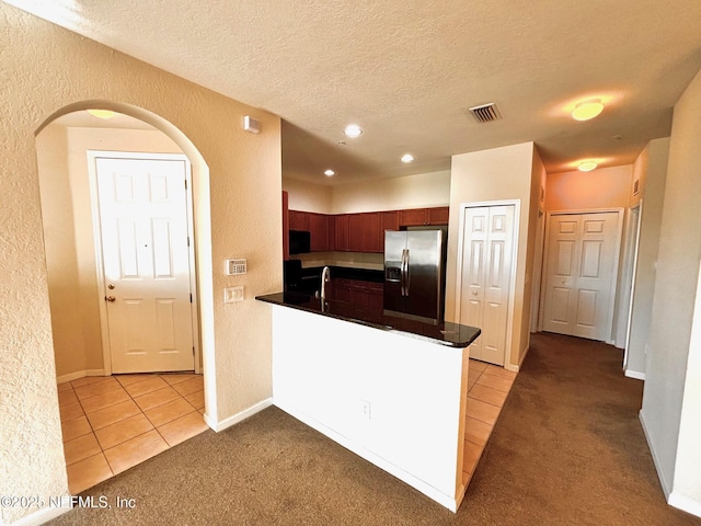 kitchen with kitchen peninsula, stainless steel fridge, light tile patterned flooring, a textured ceiling, and sink