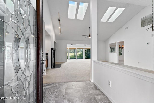 hallway with light carpet, a skylight, and high vaulted ceiling