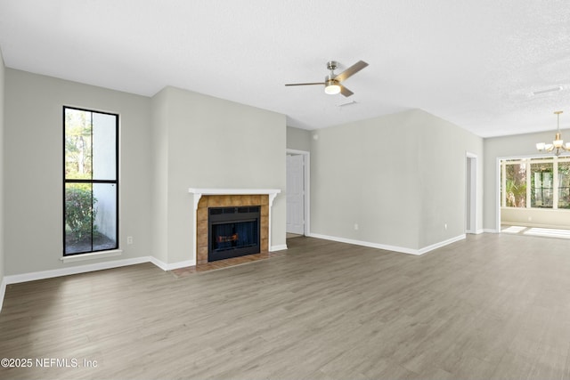 unfurnished living room featuring ceiling fan with notable chandelier, hardwood / wood-style floors, a tile fireplace, and a textured ceiling