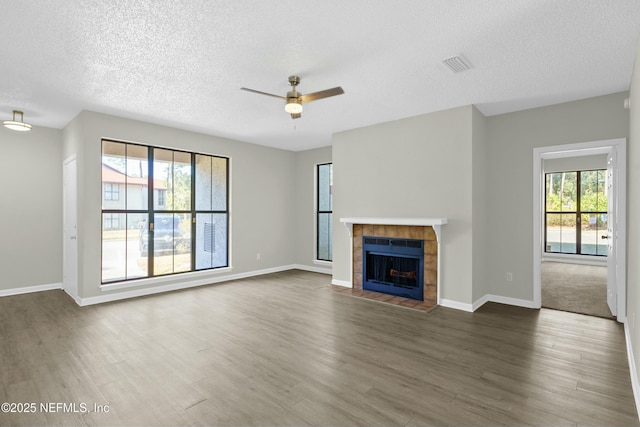 unfurnished living room featuring ceiling fan, a healthy amount of sunlight, a fireplace, and a textured ceiling