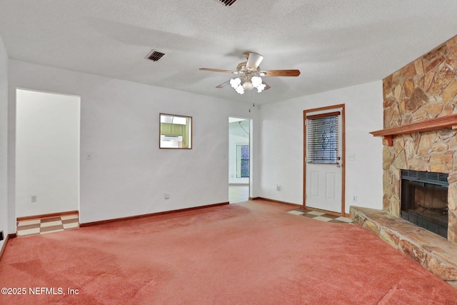 unfurnished living room featuring ceiling fan, carpet flooring, a stone fireplace, and a textured ceiling