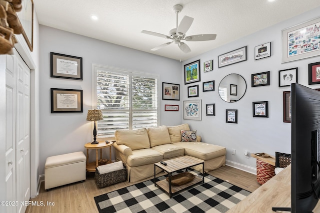 living room with a textured ceiling, ceiling fan, and light hardwood / wood-style flooring