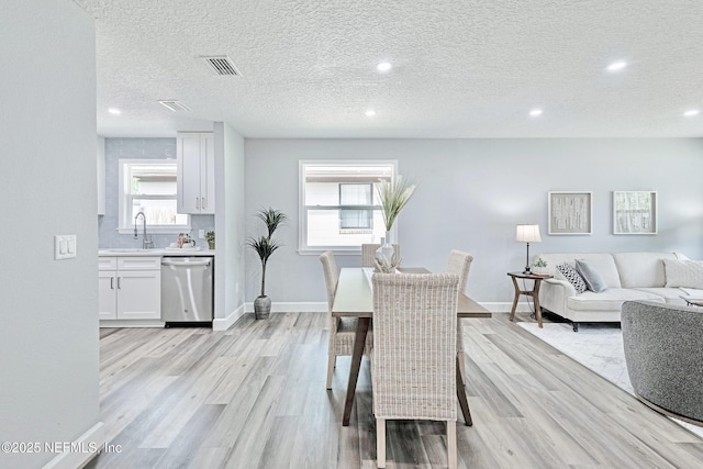 dining area featuring sink, a textured ceiling, plenty of natural light, and light wood-type flooring