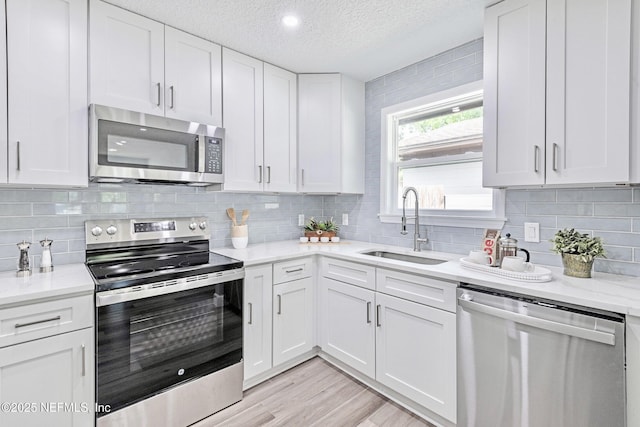 kitchen with light stone countertops, a textured ceiling, white cabinets, stainless steel appliances, and sink