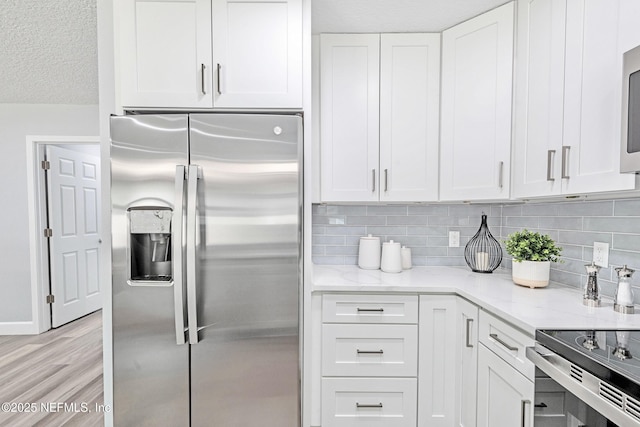 kitchen with light hardwood / wood-style floors, stainless steel fridge, backsplash, white cabinets, and light stone counters