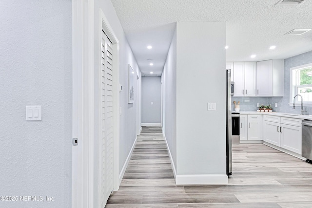 hallway with a textured ceiling, light hardwood / wood-style floors, and sink