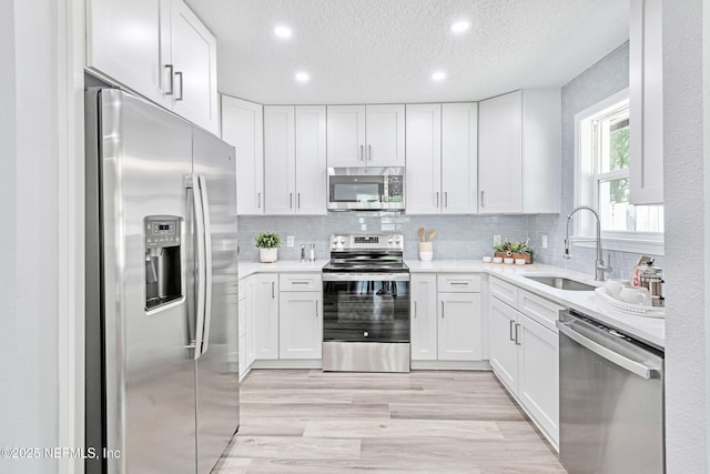 kitchen featuring a textured ceiling, appliances with stainless steel finishes, white cabinetry, sink, and light hardwood / wood-style flooring