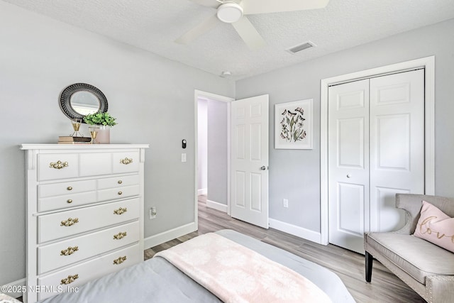 bedroom with ceiling fan, light hardwood / wood-style floors, a textured ceiling, and a closet