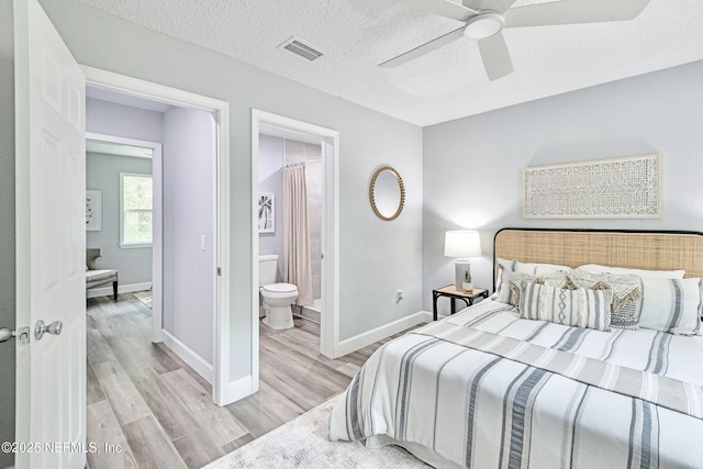 bedroom featuring ceiling fan, light wood-type flooring, ensuite bathroom, and a textured ceiling